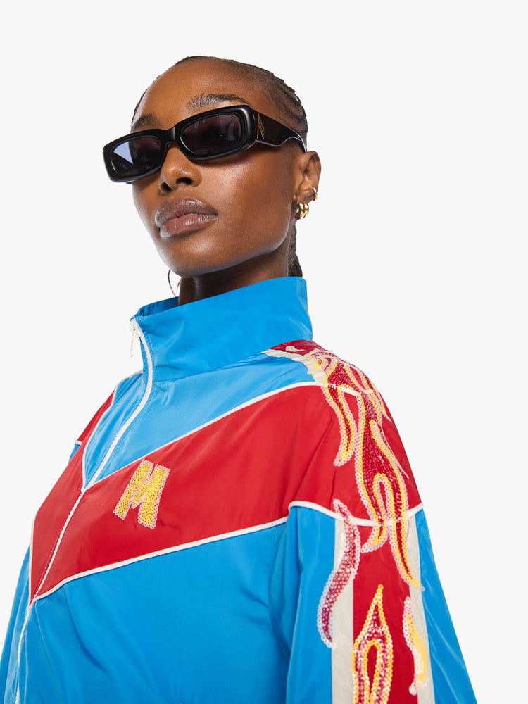Close up view of a woman in a glossy vintage blue letterman jacket with angled red panels across the chest, stripes down the sleeves, an M patch in yellow on the front and stitched details along the shoulders.