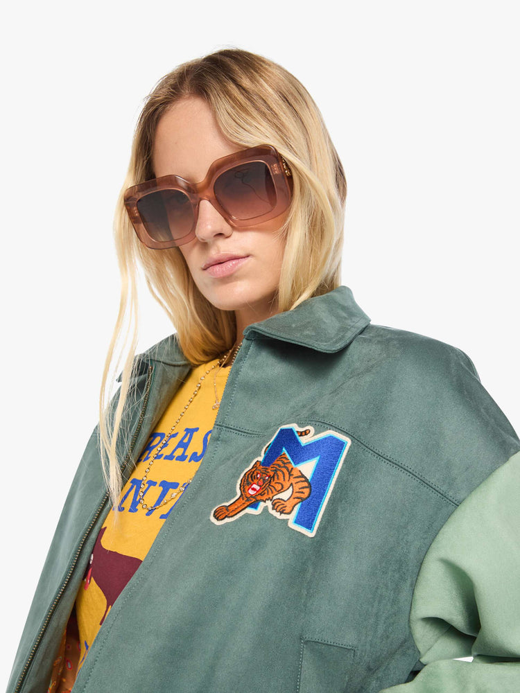 Close up view of a woman in a mint green oversized letterman jacket with drop shoulders, slit pockets, ribbed hems and a boxy fit.