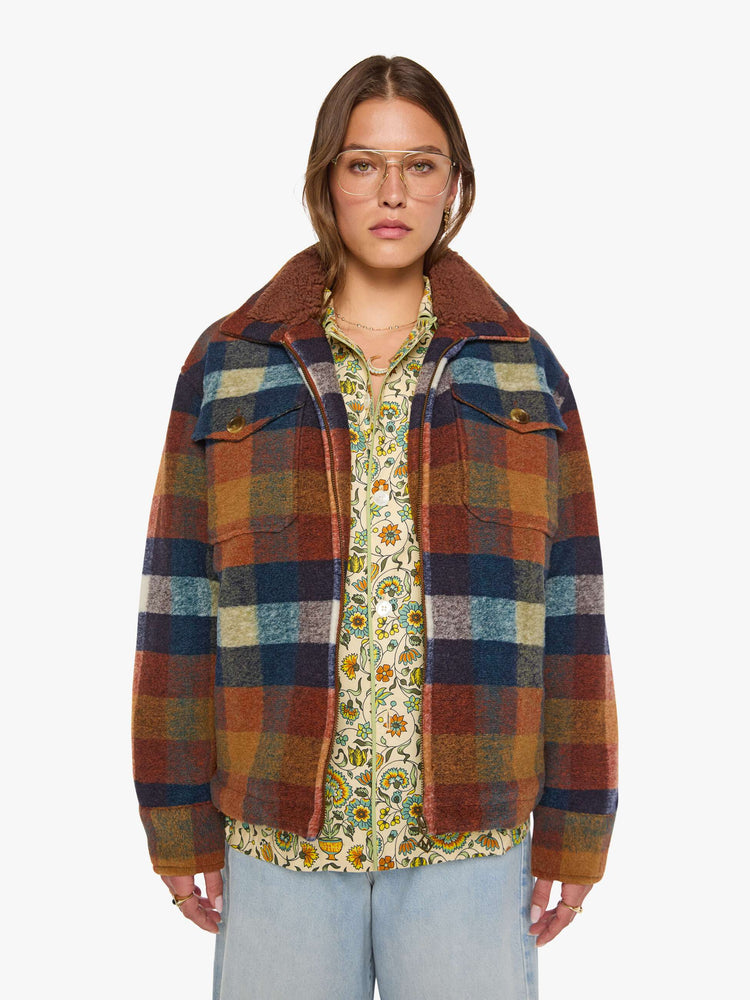 Front view of a woman in a brick red, navy, yellow and white plaid print with fuzzy faux-sherpa lining on the collared jacket with front patch pockets, a zip closure, drop shoulders and an oversized fit.