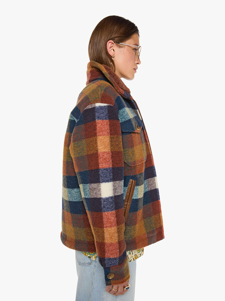 Side view of a woman in a brick red, navy, yellow and white plaid print with fuzzy faux-sherpa lining on the collared jacket with front patch pockets, a zip closure, drop shoulders and an oversized fit.