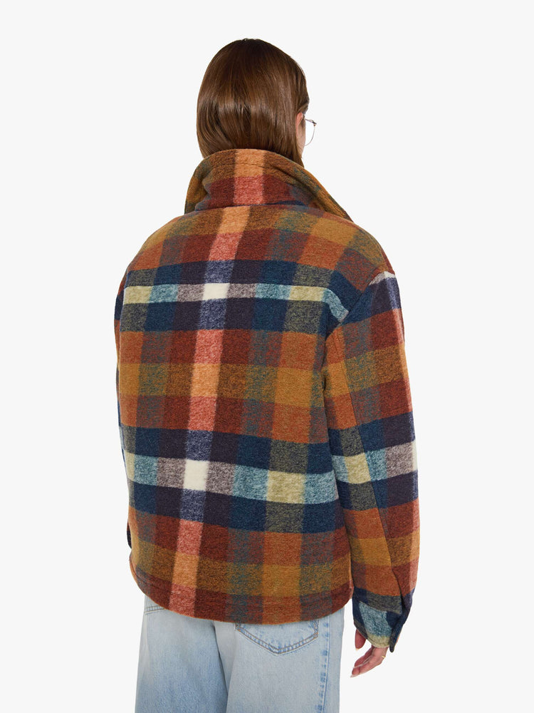 Back view of a woman in a brick red, navy, yellow and white plaid print with fuzzy faux-sherpa lining on the collared jacket with front patch pockets, a zip closure, drop shoulders and an oversized fit.