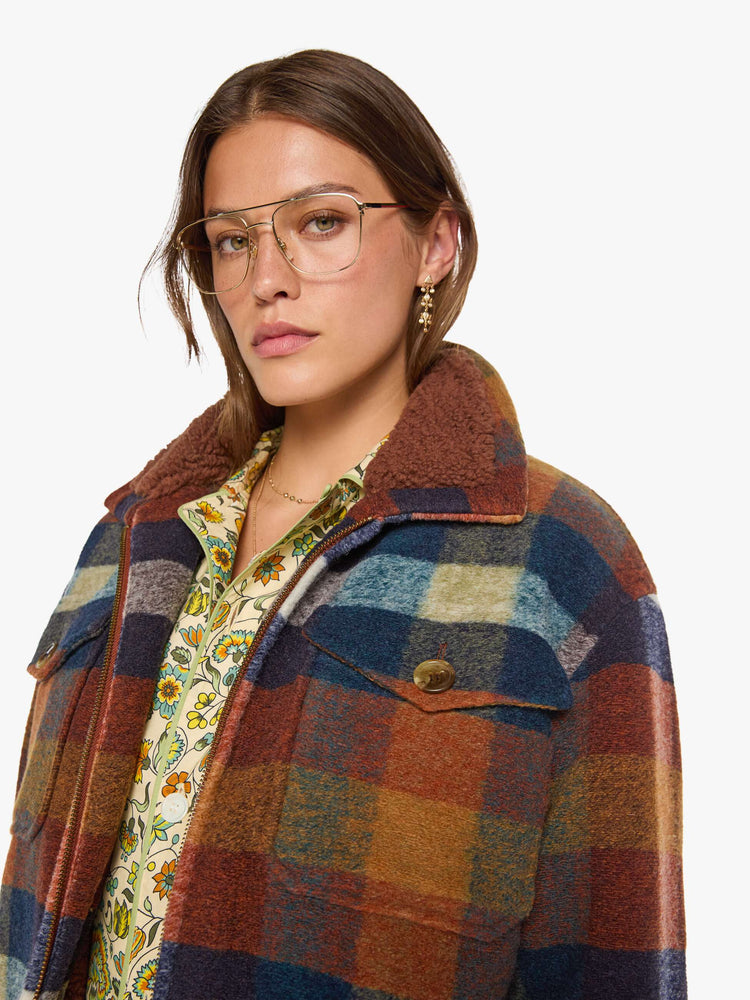 Clos up view of a woman in a brick red, navy, yellow and white plaid print with fuzzy faux-sherpa lining on the collared jacket with front patch pockets, a zip closure, drop shoulders and an oversized fit.