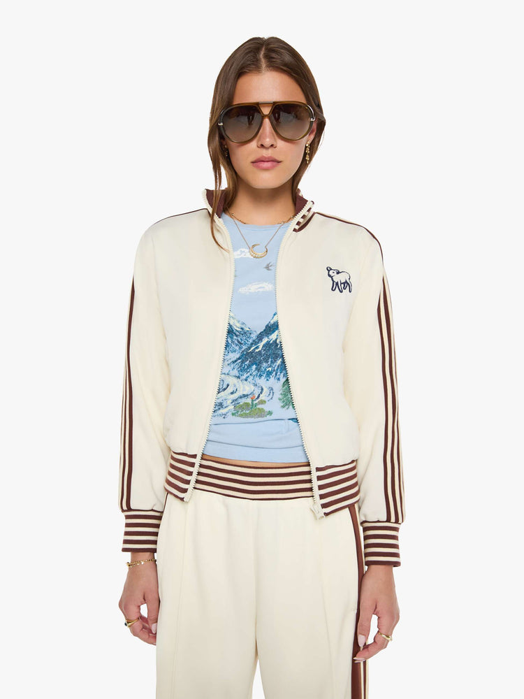 Front view of a woman in an off-white the jacket features brown and white stripes down the sleeves and at the hems and a fuzzy lamb patch on the chest.