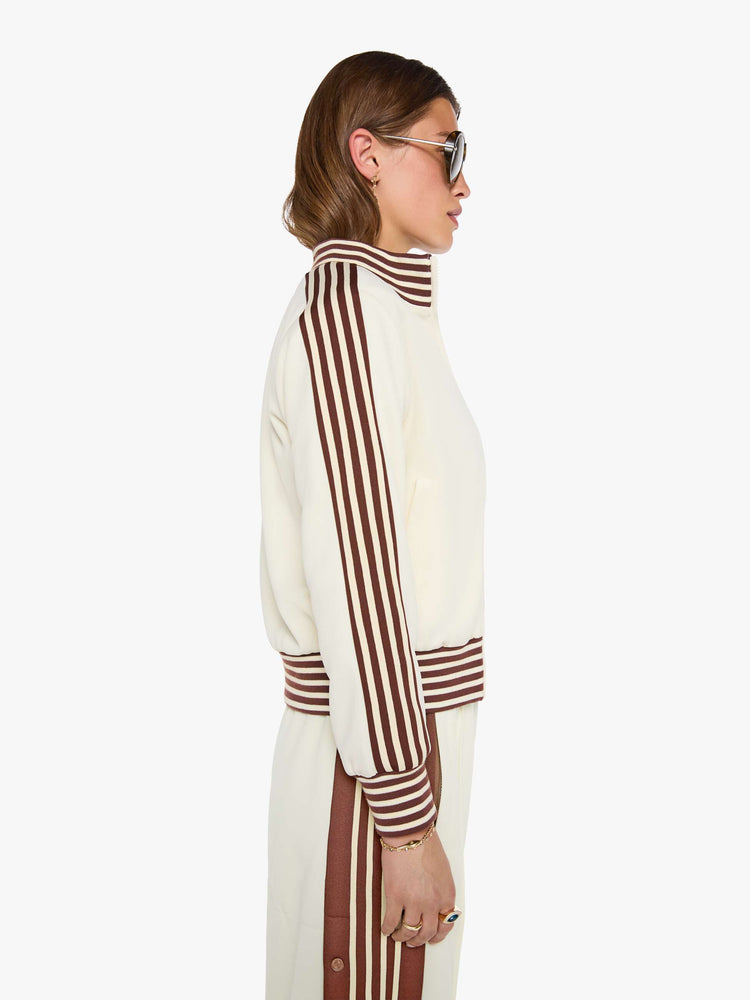 Side view of a woman in an off-white the jacket features brown and white stripes down the sleeves and at the hems and a fuzzy lamb patch on the chest.
