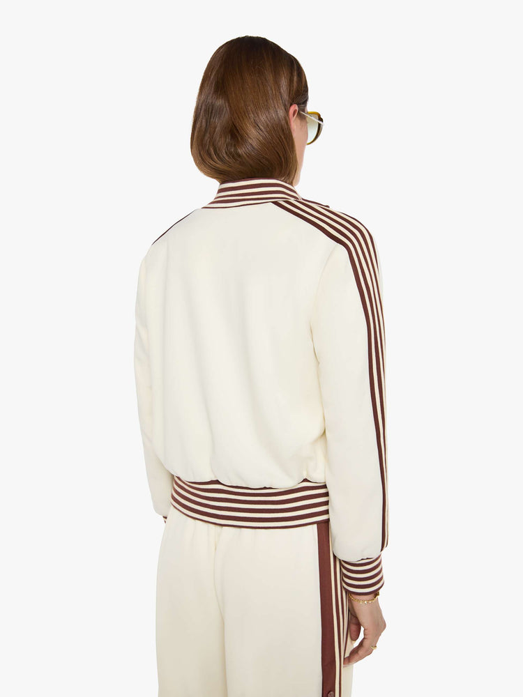 Back view of a woman in an off-white the jacket features brown and white stripes down the sleeves and at the hems and a fuzzy lamb patch on the chest.