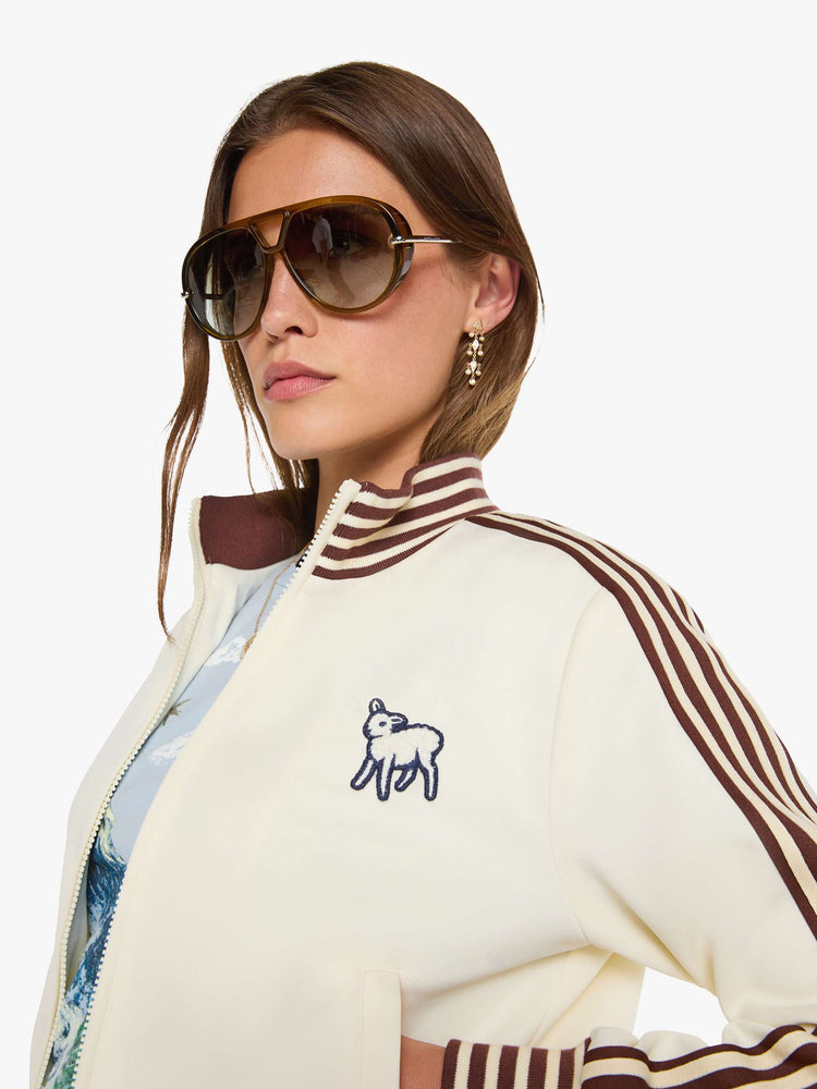 Swatch view of a woman in an off-white the jacket features brown and white stripes down the sleeves and at the hems and a fuzzy lamb patch on the chest.