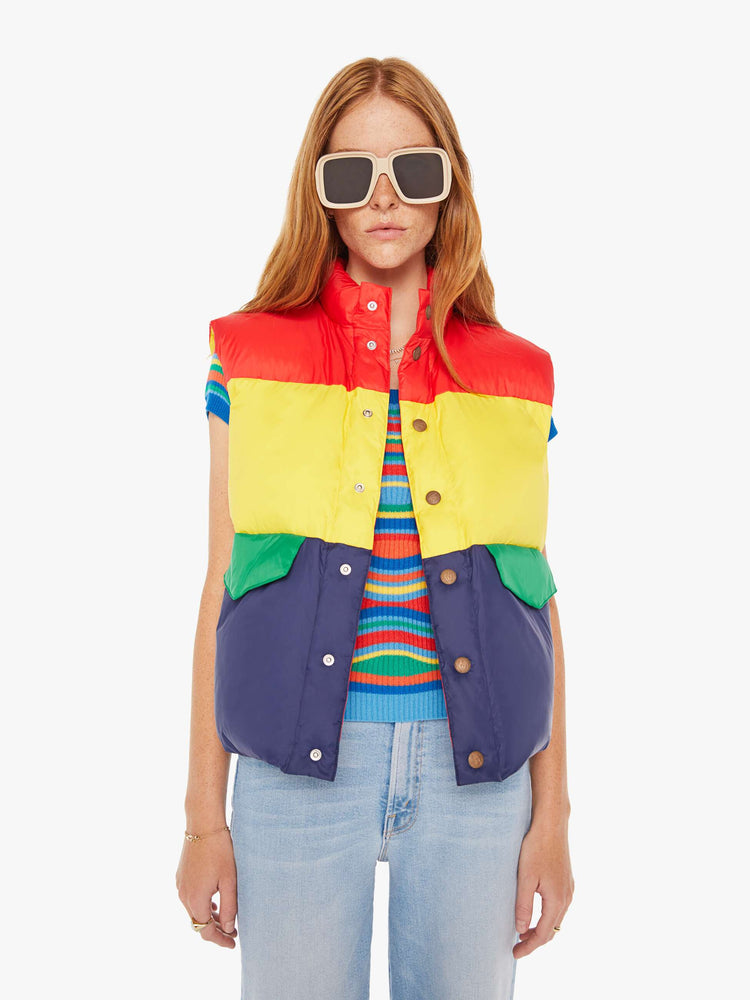 Front view of a woman puffer vest with a funnel neck, snaps down the front and patch pockets in shades of red, yellow and navy with green details at pockets.