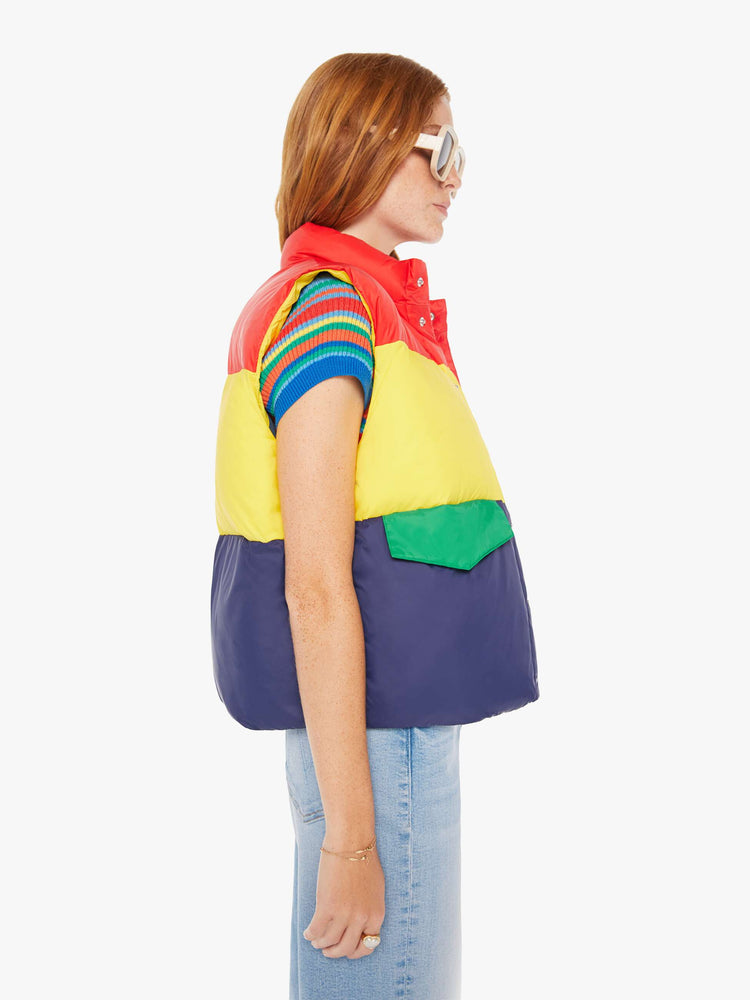 Side view of a woman puffer vest with a funnel neck, snaps down the front and patch pockets in shades of red, yellow and navy with green details at pockets.