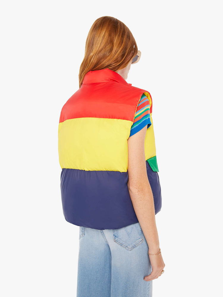 Back view of a woman puffer vest with a funnel neck, snaps down the front and patch pockets in shades of red, yellow and navy with green details at pockets.
