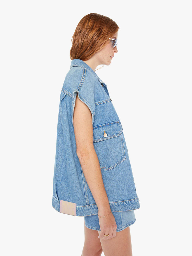 Side view of a womens light blue denim vest featuring an oversized fit.