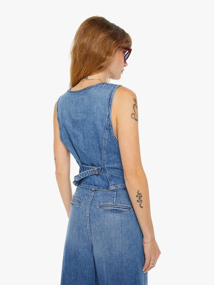 Back view of a woman medium blue deep V-neck, three-button closure, slit pockets and an adjustable tab in the back.