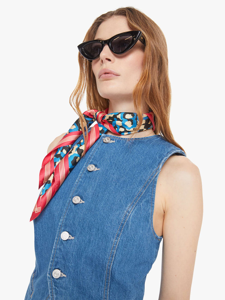 Close up view of a woman in a med blue denim vest with a crewneck, buttons down the front, slit pockets and angled seams.