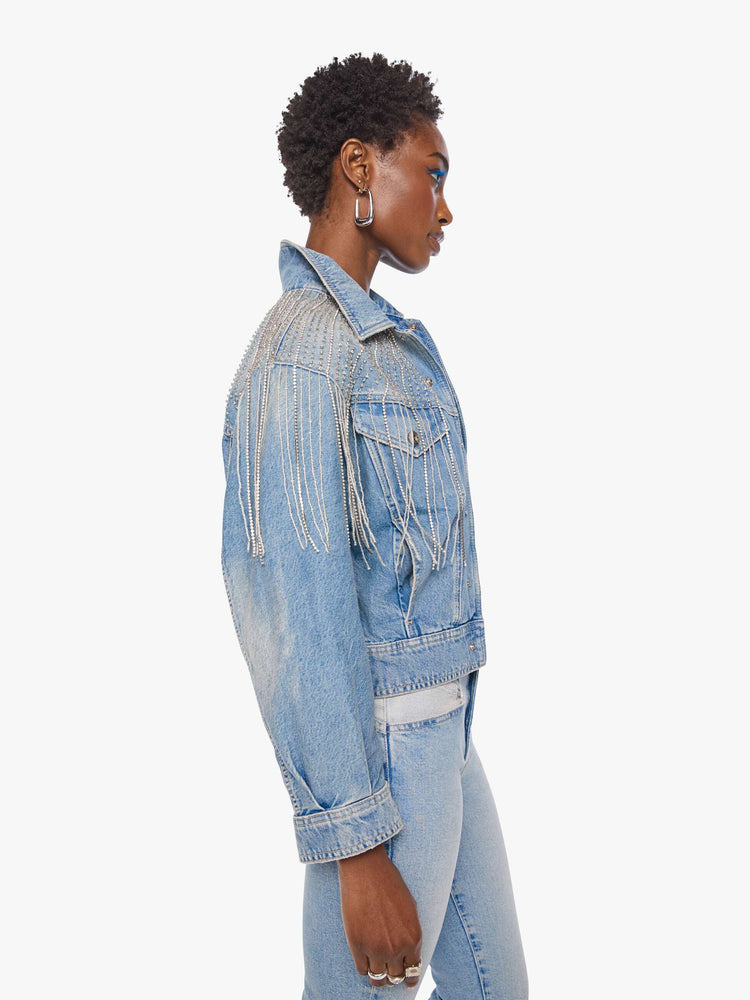 Side view of a woman in a light blue  jacket with fading on the chest and elbows and glittery fringe around the neck.