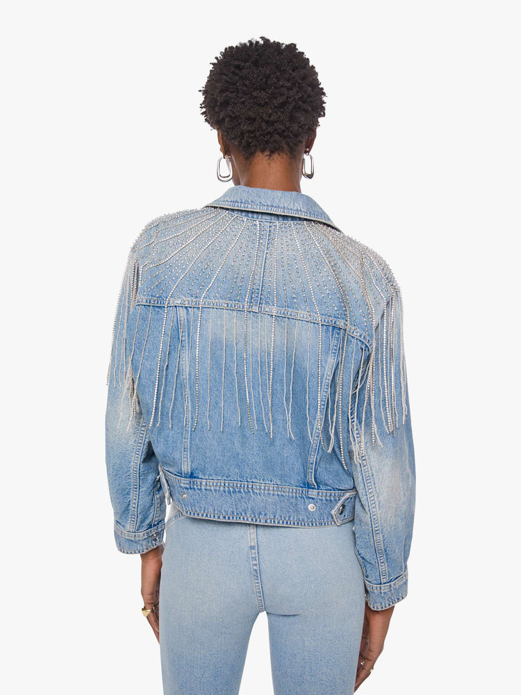 Back view of a woman in a light blue  jacket with fading on the chest and elbows and glittery fringe around the neck.