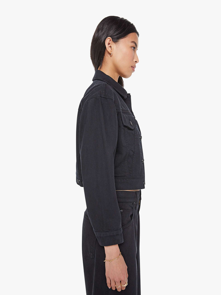 Side view of a woman in a black shrunken denim jacket with drop shoulders, front patch pockets and a cropped fit. 