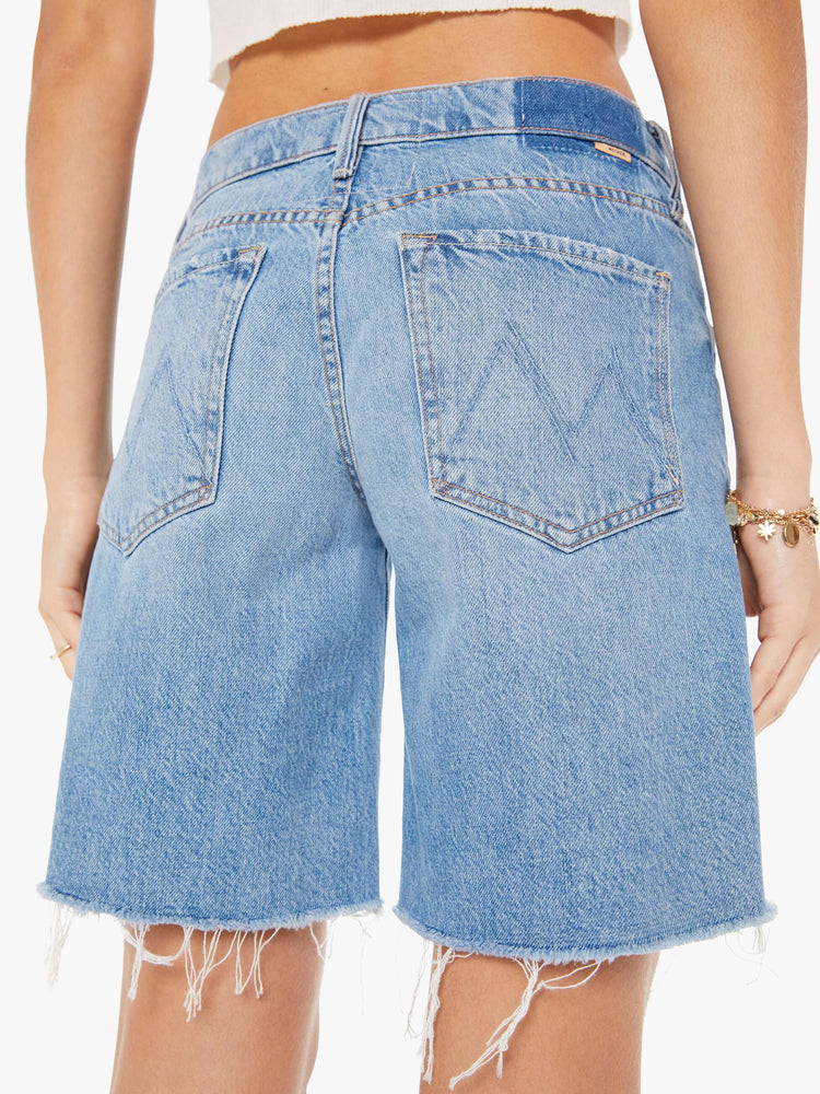 Back close up view of a woman wearing a light blue wash denim short featuring a low rise and a relaxed fit with a long raw hem inseam.