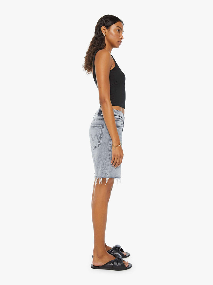 Side view of a woman in light-grey low-rise frayed hem denim shorts with whiskering and fading.