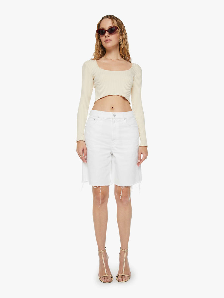 Front view of a woman in off-white shorts that have a super-high rise, loose leg with a frayed hem and a pretzel-detailed button.