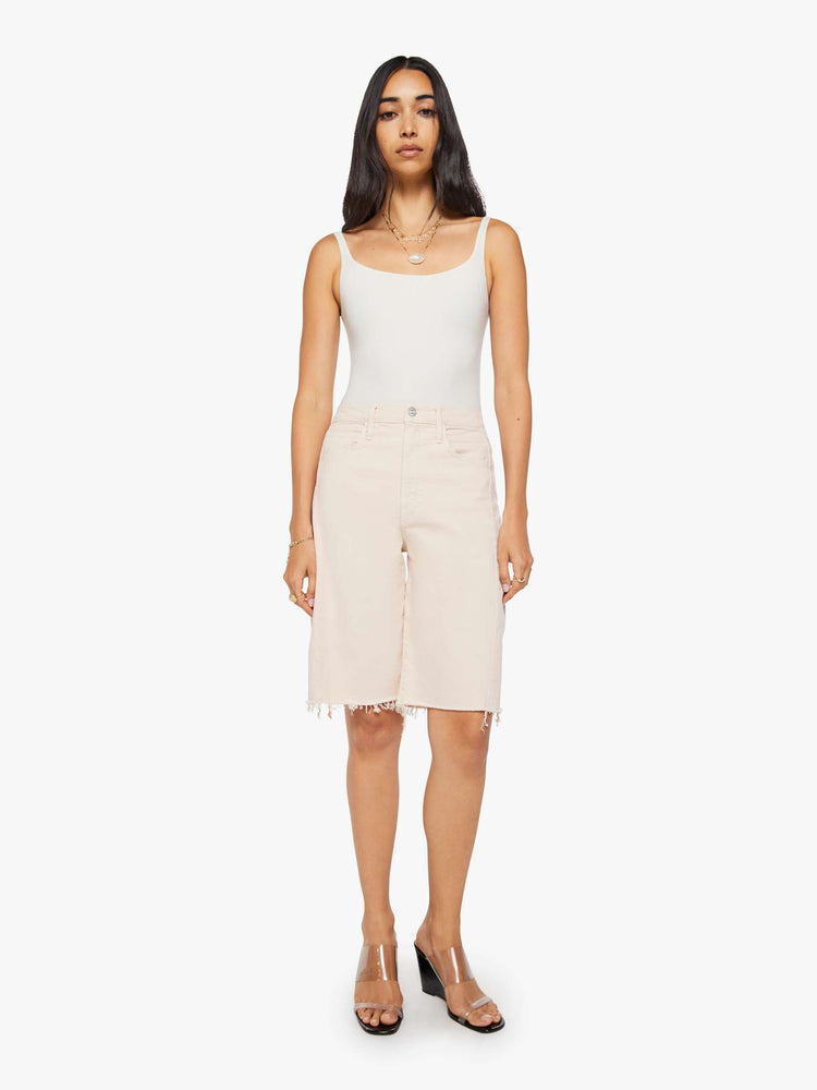 Front view of a woman in pure peach super high-waisted bermuda shorts with a zip fly, wide leg, knee-length inseam and a frayed hem.