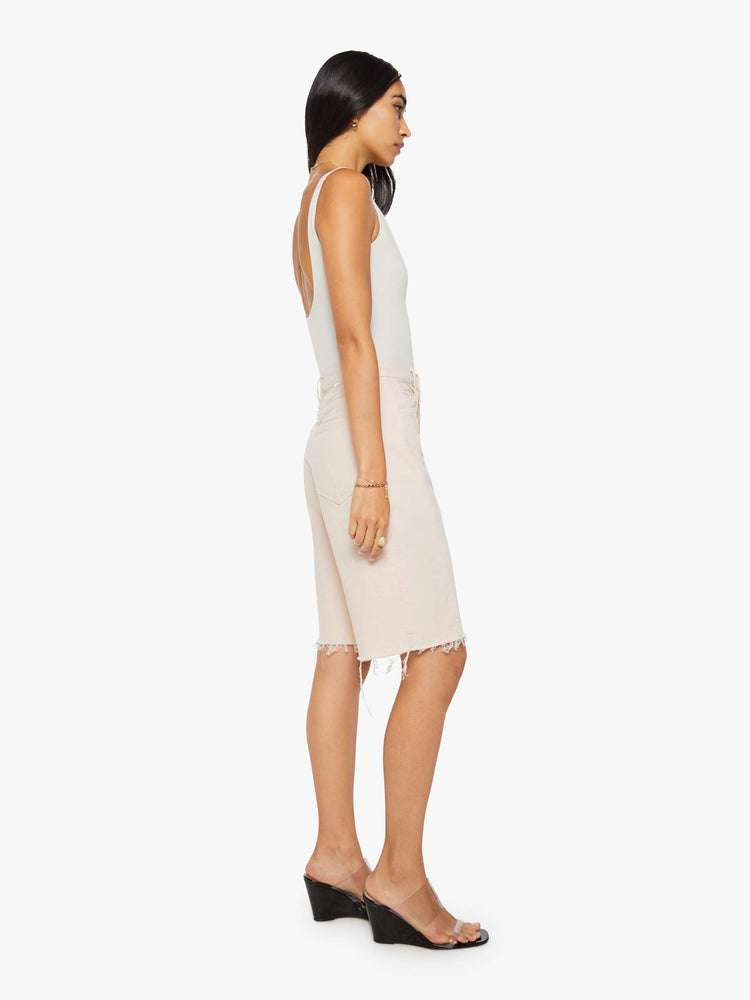 Side view of a woman in pure peach super high-waisted bermuda shorts with a zip fly, wide leg, knee-length inseam and a frayed hem.