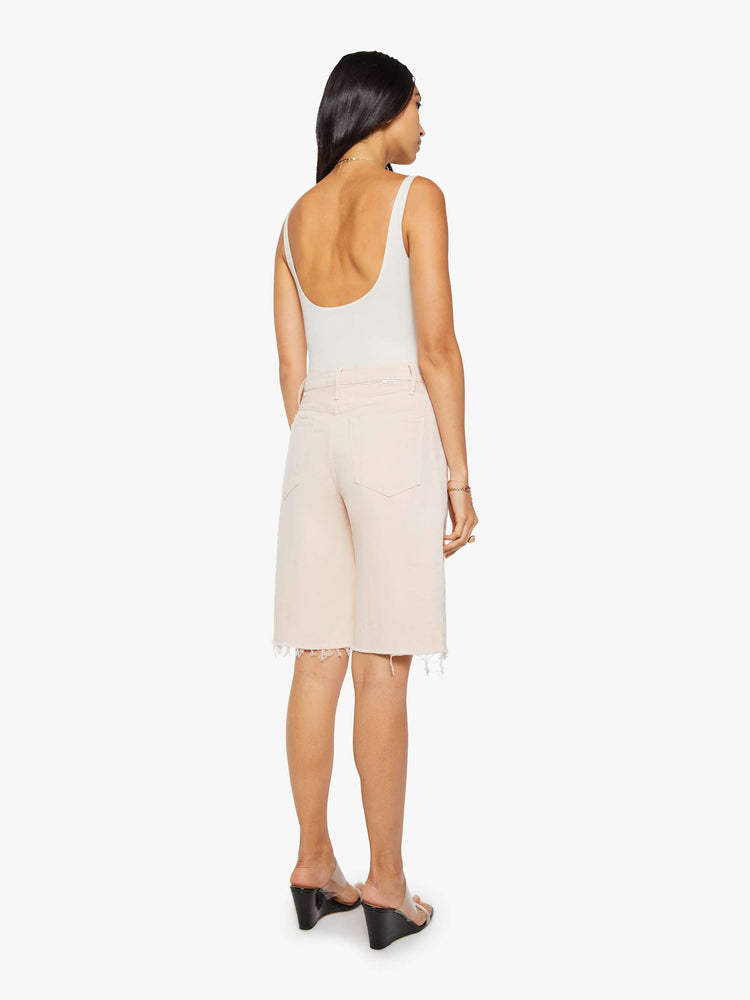 Back view of a woman in pure peach super high-waisted bermuda shorts with a zip fly, wide leg, knee-length inseam and a frayed hem.
