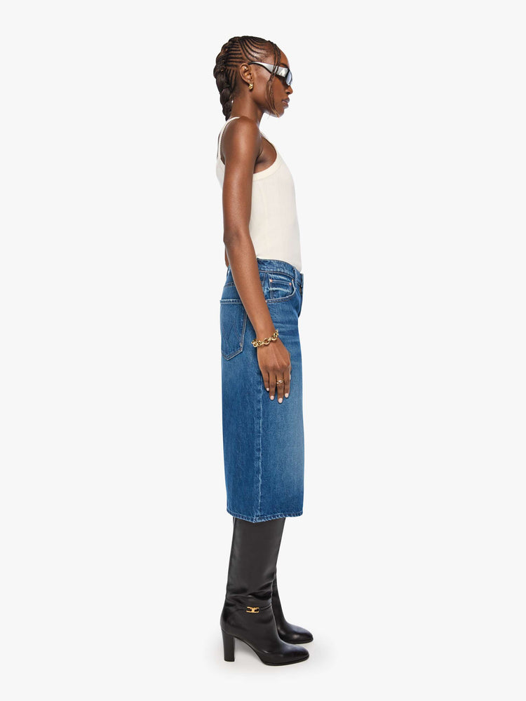 Side view of woman in med blue high-waisted shorts have a low-slung fit and feature a wide leg, zip fly, calf-length inseam and a clean hem.