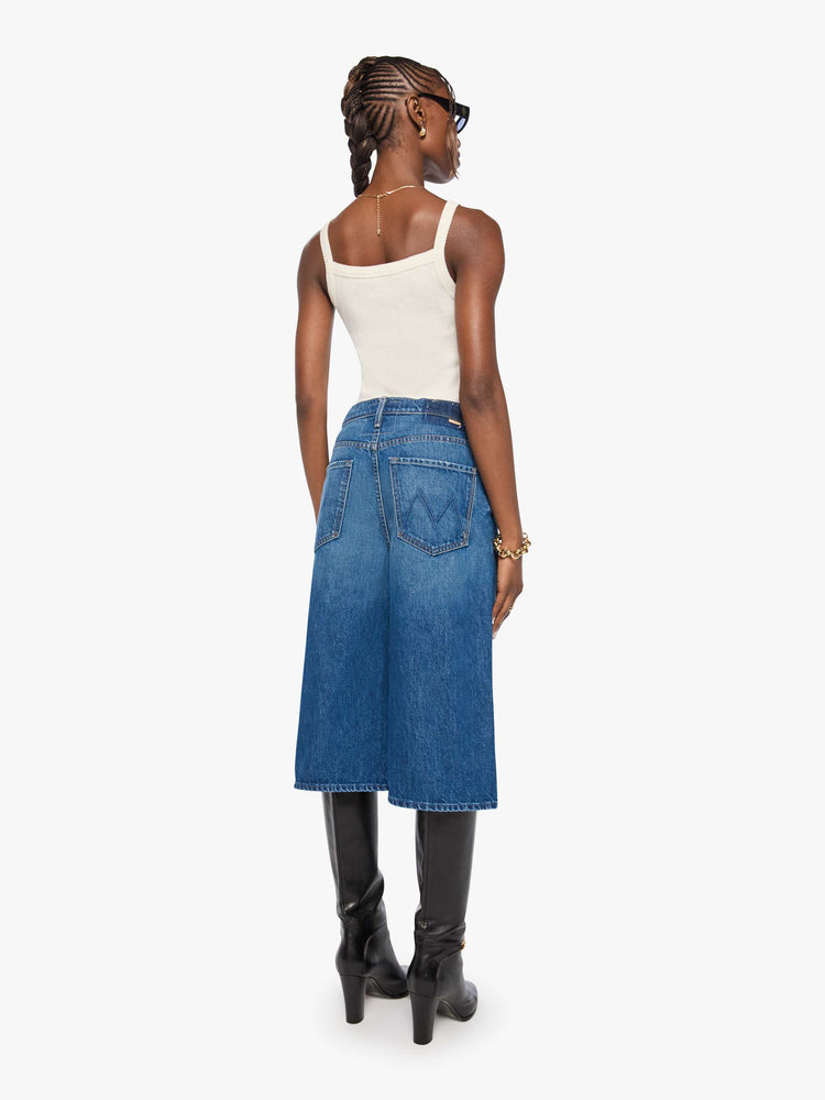 Back view of woman in med blue high-waisted shorts have a low-slung fit and feature a wide leg, zip fly, calf-length inseam and a clean hem.