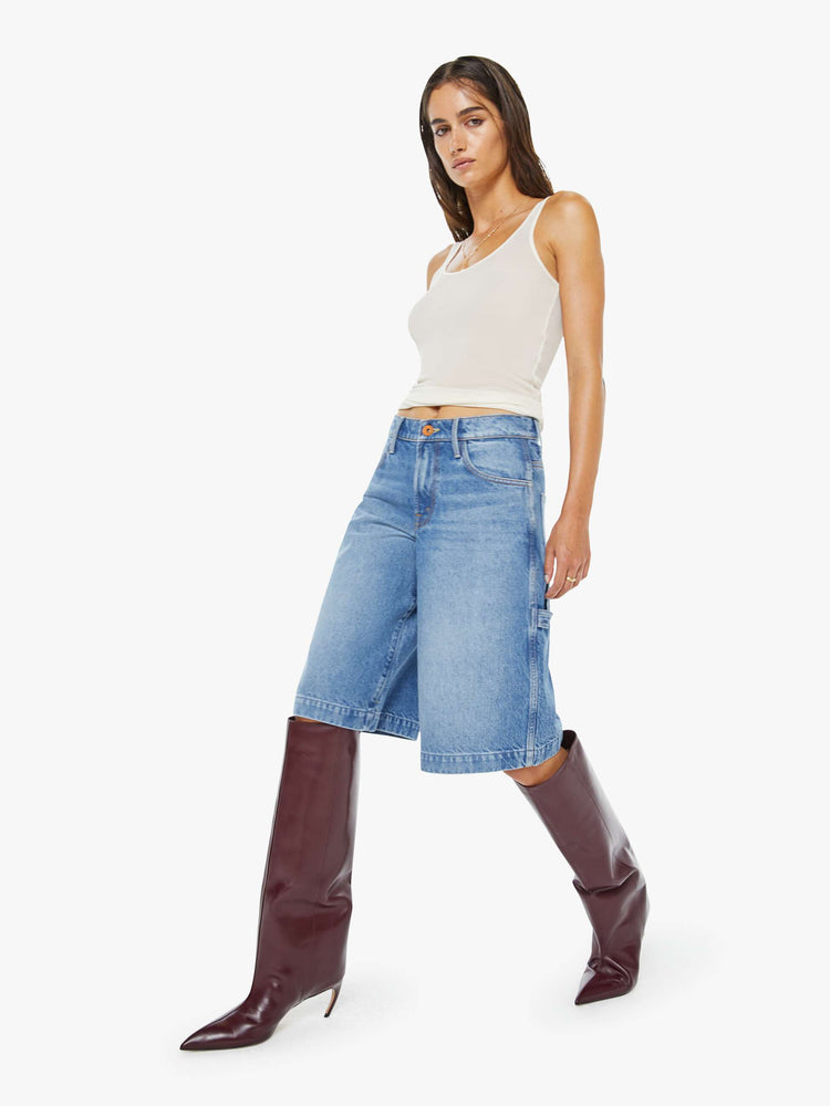 Walking view of a woman in a mid blue mid-waisted shorts have a low-slung fit, zip fly, loose wide-leg and a 15-inch inseam with a clean hem.