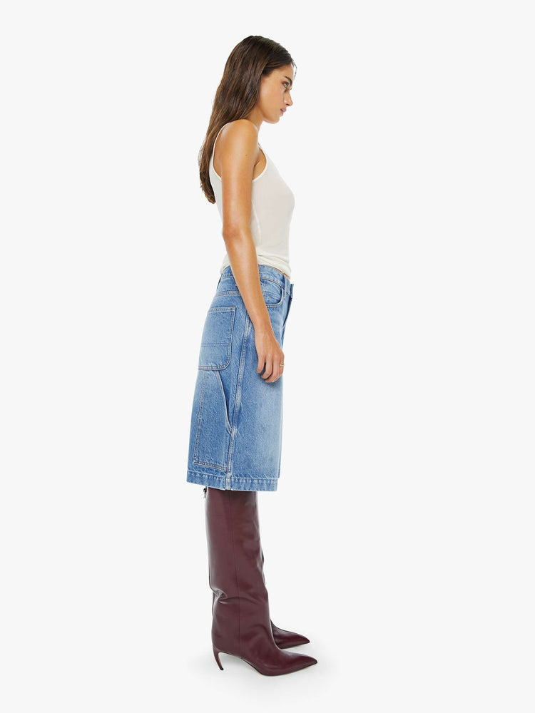 Side view of a woman in a mid blue mid-waisted shorts have a low-slung fit, zip fly, loose wide-leg and a 15-inch inseam with a clean hem.