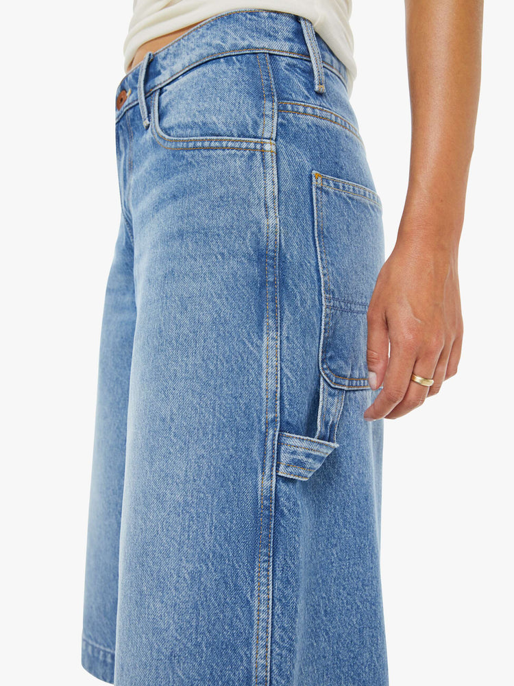 Close up view of a woman in a mid blue mid-waisted shorts have a low-slung fit, zip fly, loose wide-leg and a 15-inch inseam with a clean hem.