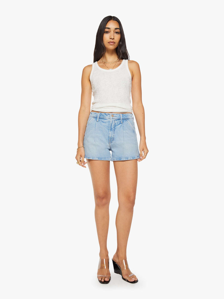Front view of a woman in a light blue high-waisted denim shorts with a zip fly, slit pockets, pleats at the waistband and a 3-inch inseam with a clean hem.