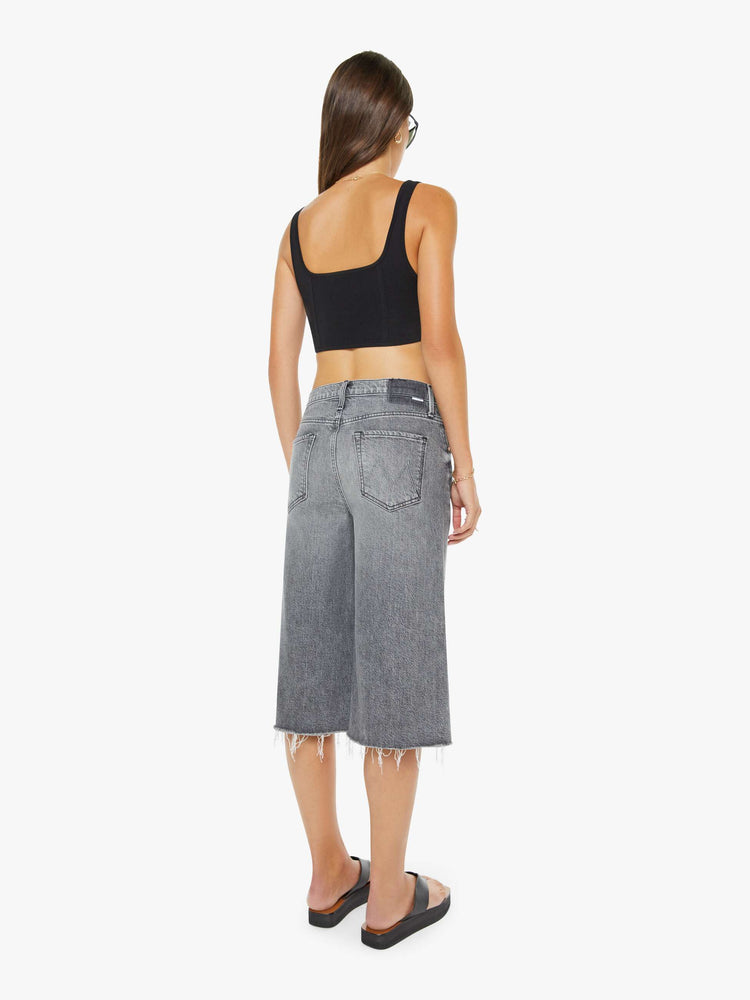 Back view of a woman in a light grey super high-waisted shorts with a wide leg, zip fly, calf-length inseam and a frayed hem.