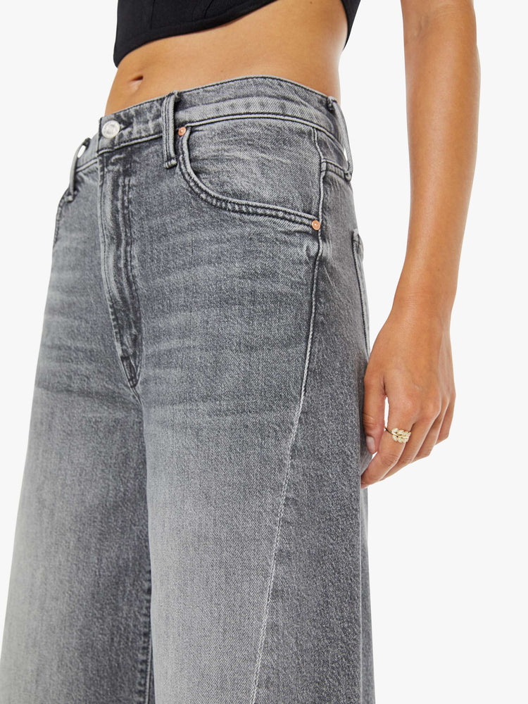 Close up view of a woman in a light grey super high-waisted shorts with a wide leg, zip fly, calf-length inseam and a frayed hem.