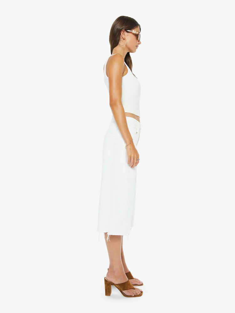 Side view of a woman in a white super high-waisted shorts with a wide leg, zip fly, calf-length inseam and a frayed hem.