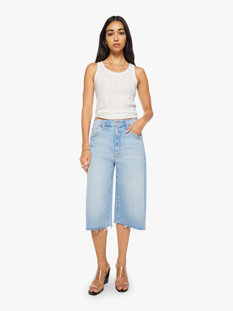 Front view of a woman in a light blue high-waisted shorts have a low-slung fit and feature a wide leg, zip fly, calf-length inseam and a frayed hem.