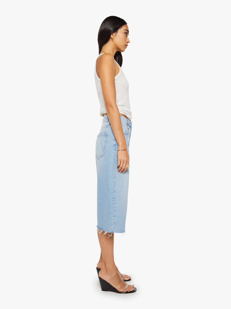 Side view of a woman in a light blue high-waisted shorts have a low-slung fit and feature a wide leg, zip fly, calf-length inseam and a frayed hem.