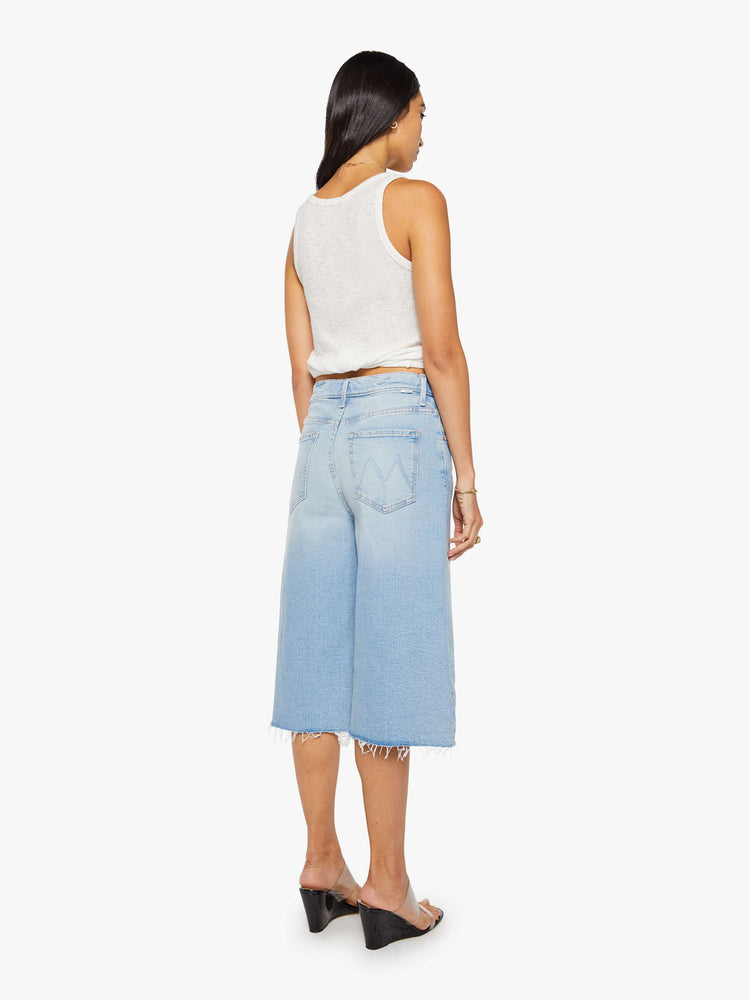Back view of a woman in a light blue high-waisted shorts have a low-slung fit and feature a wide leg, zip fly, calf-length inseam and a frayed hem.