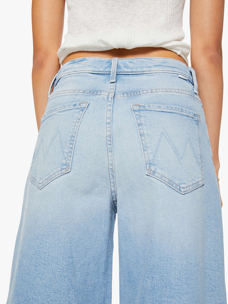 Close up view of a woman in a light blue high-waisted shorts have a low-slung fit and feature a wide leg, zip fly, calf-length inseam and a frayed hem.