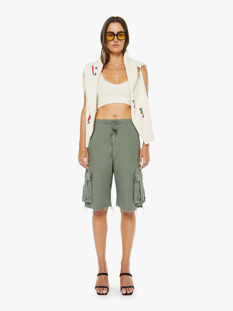 Front view of a woman in an army green shorts with a drawstring waist, zip fly, patch pockets on the thighs and a knee-length inseam with a frayed hem.