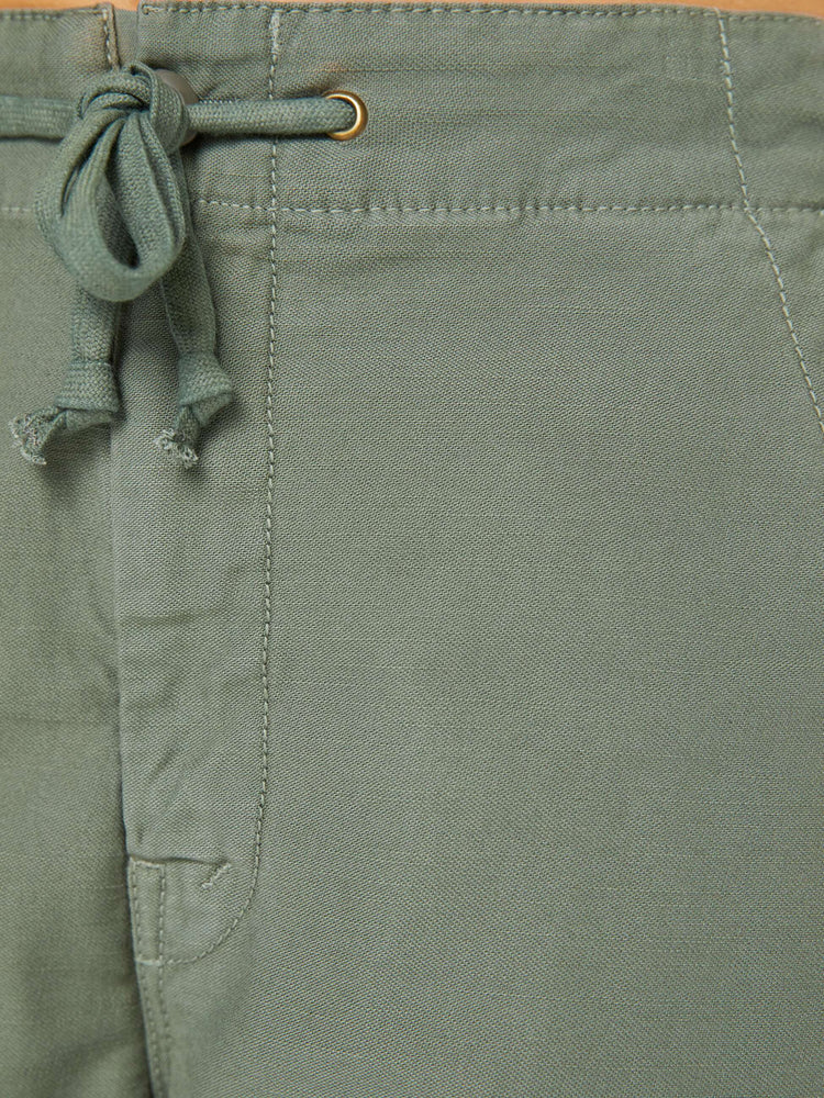Swatch view of a woman in an army green shorts with a drawstring waist, zip fly, patch pockets on the thighs and a knee-length inseam with a frayed hem.