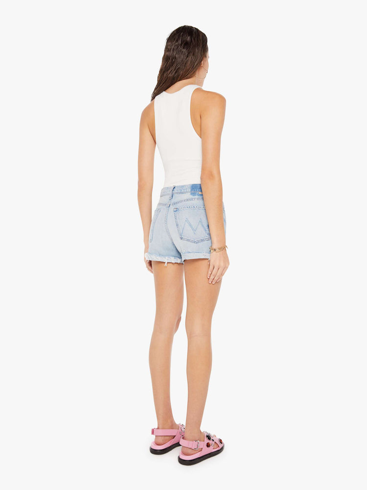 A back full body view of a woman wearing a light blue wash denim short featuring a high rise and a cuffed raw hem, paired with a white tank.