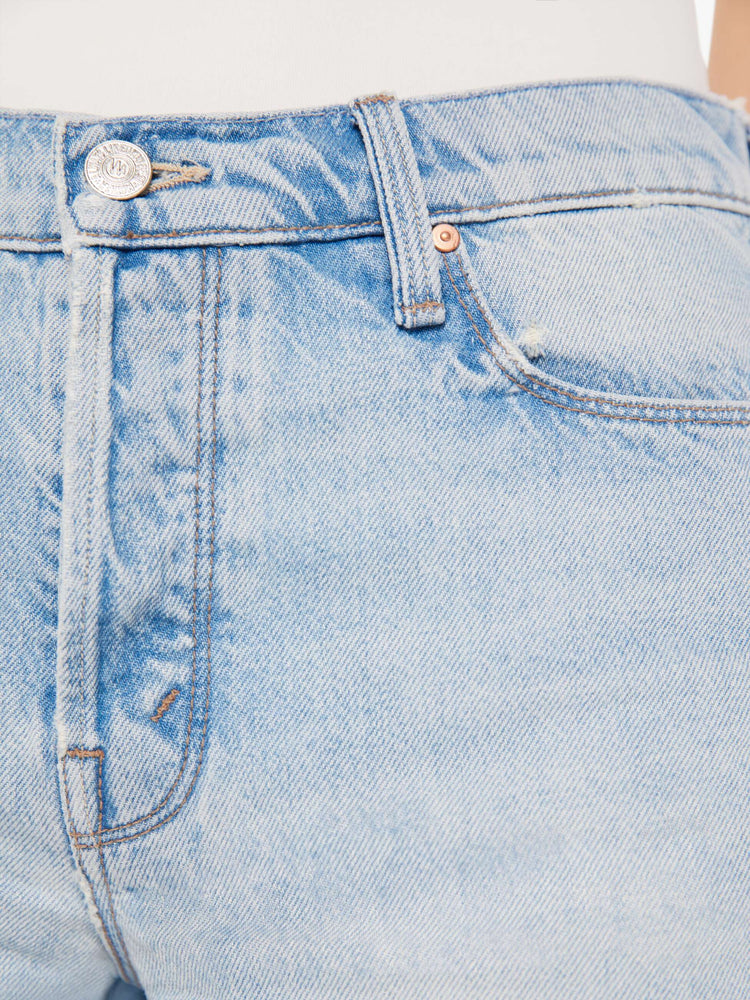 A close up detail swatch view of a light blue wash jean featuring silver and copper hardware with contrast brown thread.