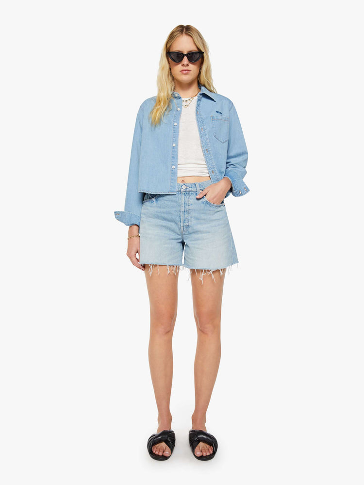 Front view of a woman in a light blue super high-waisted denim shorts with a zip fly, 4.75-inch inseam, a frayed hem and a low-slung fit.