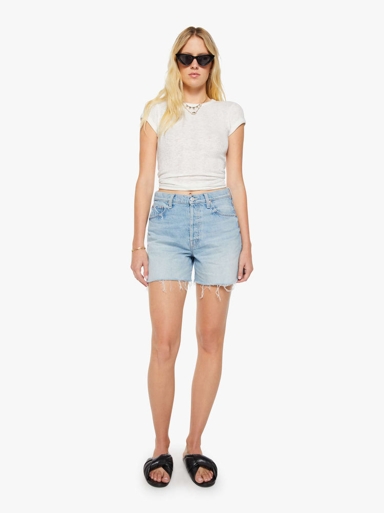 Full body view of a woman in a light blue super high-waisted denim shorts with a zip fly, 4.75-inch inseam, a frayed hem and a low-slung fit.