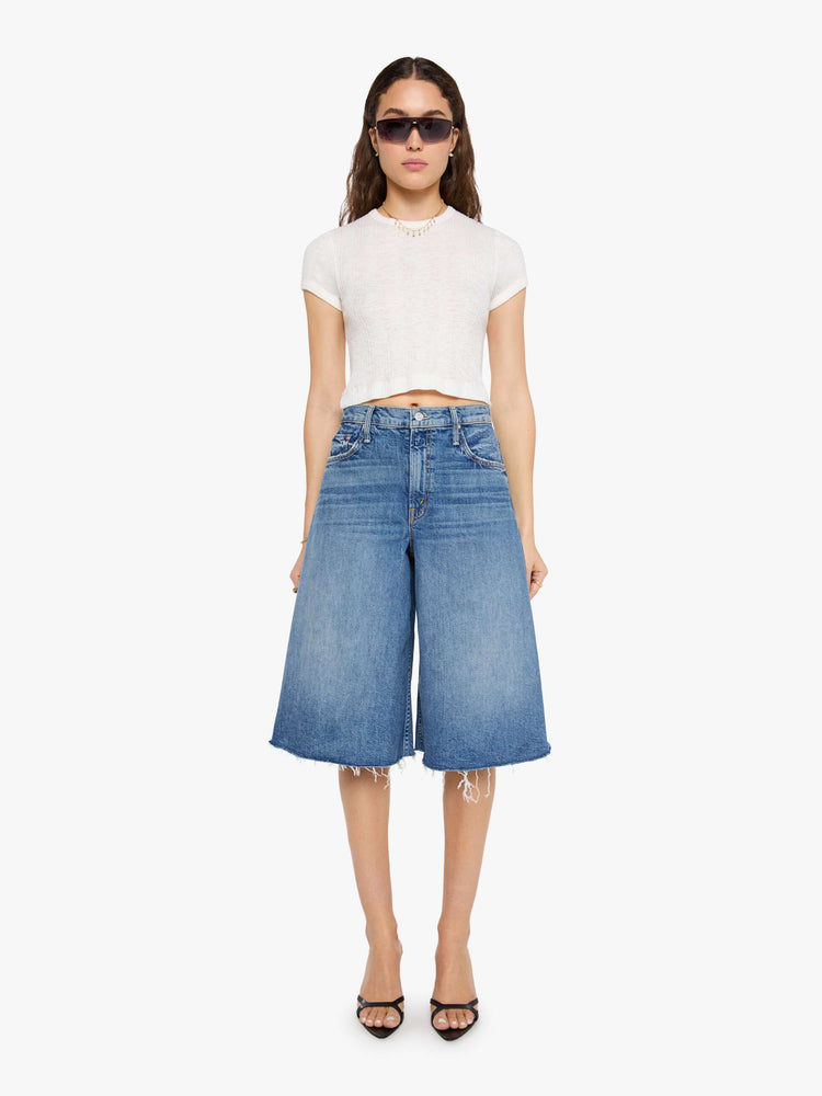 Front view of a woman in a mid blue high-waisted shorts have a low-slung fit and feature a wide leg that flares out at the knee, a zip fly, calf-length inseam and a frayed hem.