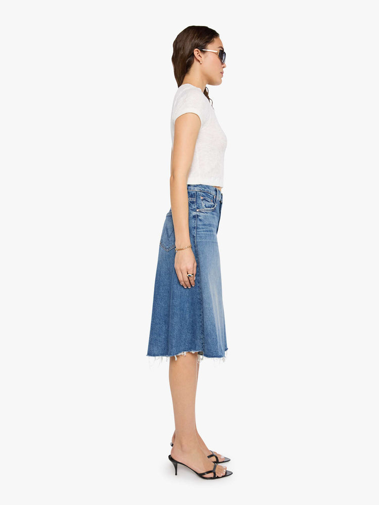 Side view of a woman in a mid blue high-waisted shorts have a low-slung fit and feature a wide leg that flares out at the knee, a zip fly, calf-length inseam and a frayed hem.