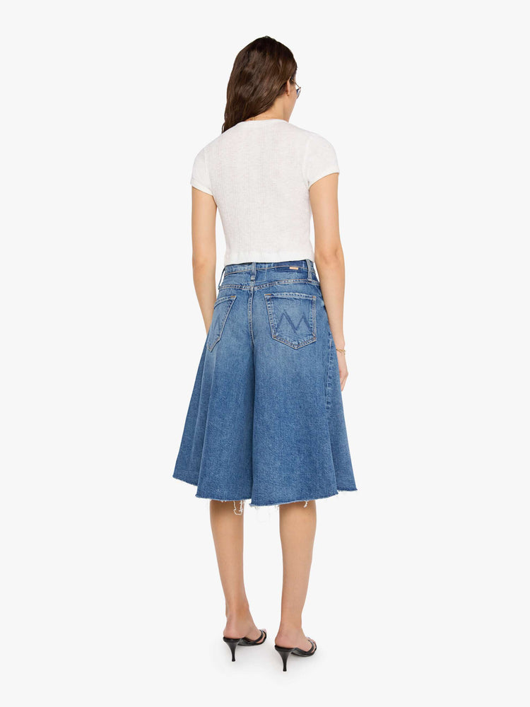 Back view of a woman in a mid blue high-waisted shorts have a low-slung fit and feature a wide leg that flares out at the knee, a zip fly, calf-length inseam and a frayed hem.