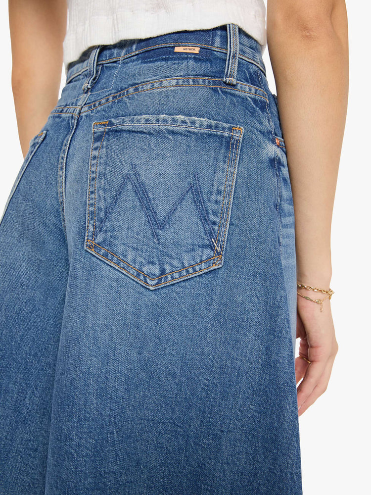 Close up view of a woman in a mid blue high-waisted shorts have a low-slung fit and feature a wide leg that flares out at the knee, a zip fly, calf-length inseam and a frayed hem.