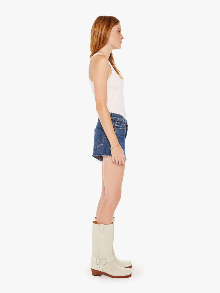 Side view of a dark blue wash denim short featuring a relaxed mid rise and a frayed hem.