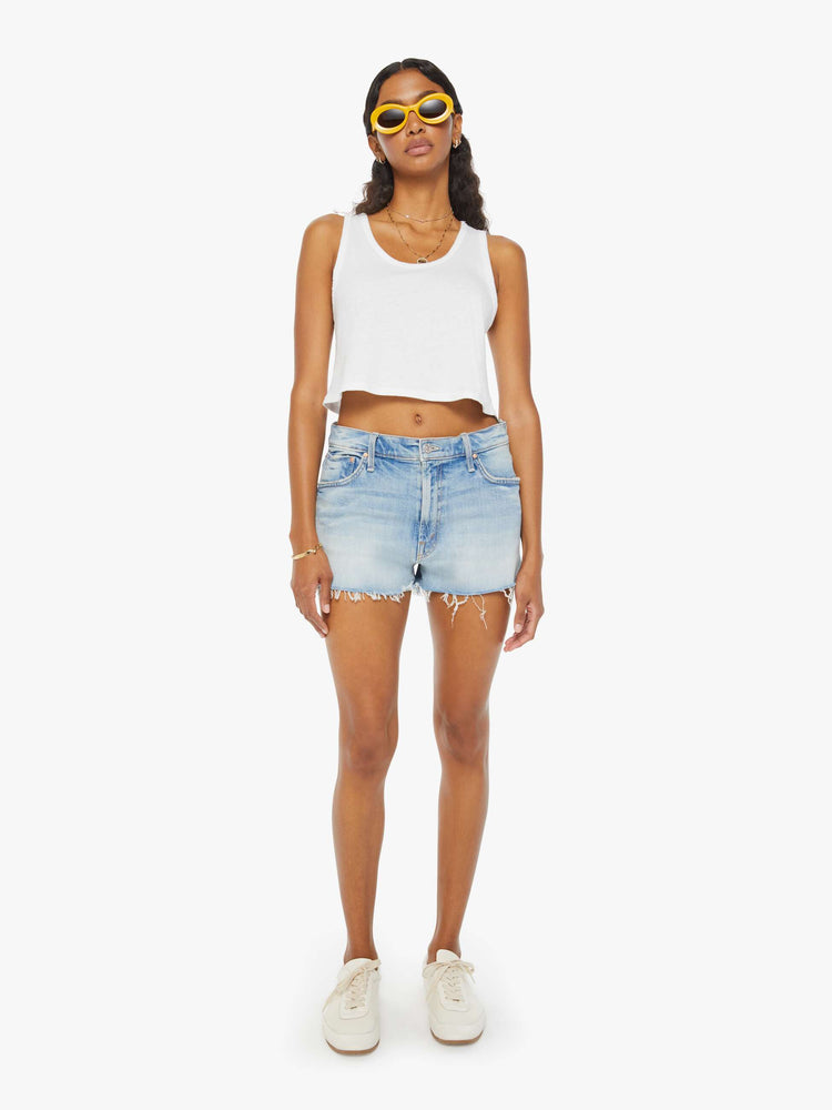 Front view of a woman in light blue denim shorts designed to sit lower on the hips with a frayed hem and whiskering, fading, and distressed details. 